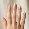 Woman's hand displaying variety of almond nail designs in elegant studio photography setup