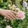 Manicured hand with baby blue nails reaching to touch a single flower bloom in garden setting