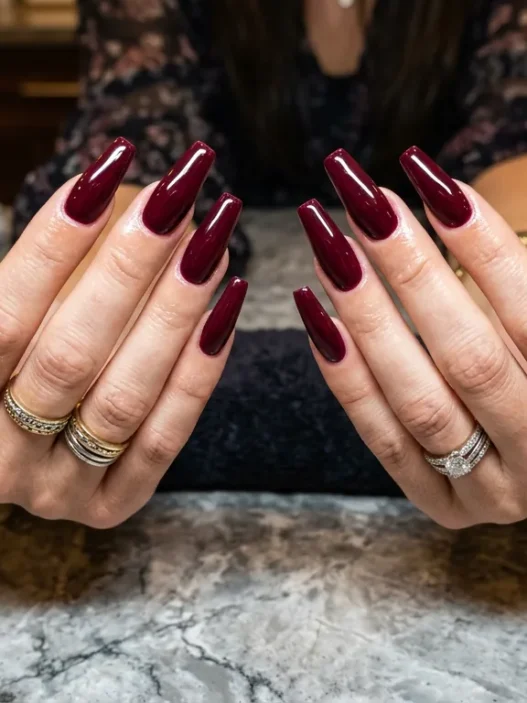 Woman's hands displaying completed long coffin baddie nails with glossy deep burgundy polish on salon table