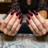 Woman's hands displaying completed long coffin baddie nails with glossy deep burgundy polish on salon table