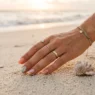 Manicured hand resting on pale beach sand with small shell and coral pieces beside fingertips