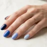 Woman's hand showing multiple blue nail polish shades arranged in gradient from light to dark