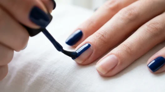 Close-up of nail brush applying glossy navy blue polish in center stroke on natural nail