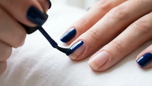 Close-up of nail brush applying glossy navy blue polish in center stroke on natural nail
