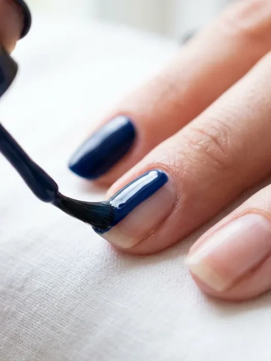 Close-up of nail brush applying glossy navy blue polish in center stroke on natural nail