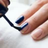 Close-up of nail brush applying glossy navy blue polish in center stroke on natural nail