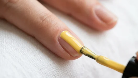 Polish brush applying butter yellow nail lacquer in single stroke down nail center with glossy ribbon of color