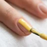 Polish brush applying butter yellow nail lacquer in single stroke down nail center with glossy ribbon of color