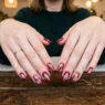 Woman's hands displaying completed Christmas nail manicure with red base and white snowflake details