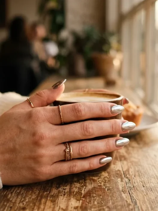 Woman's hand with metallic chrome finish nails reflecting golden light through coffee shop window
