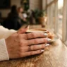 Woman's hand with metallic chrome finish nails reflecting golden light through coffee shop window
