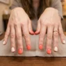 Woman's hands showing finished coral and cream summer manicure with glossy top coat on salon table
