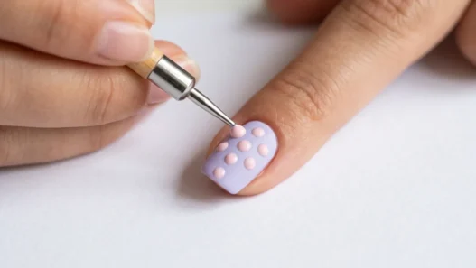 Metal dotting tool placing perfect dot of polish on pastel nail with existing dot pattern