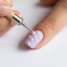 Metal dotting tool placing perfect dot of polish on pastel nail with existing dot pattern