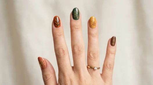 Woman's hand showing various fall nail designs in autumn colors like burnt orange, burgundy, and gold