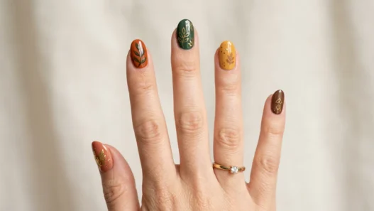 Woman's hand showing various fall nail designs in autumn colors like burnt orange, burgundy, and gold