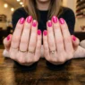 Woman's hands showing completed birthday nail design with bright pink base, gold dots and glitter accents