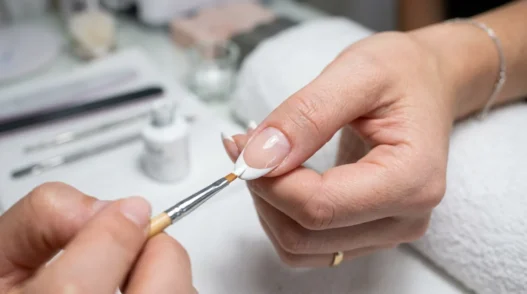 Close-up of precision brush applying white polish to create perfect French tip manicure