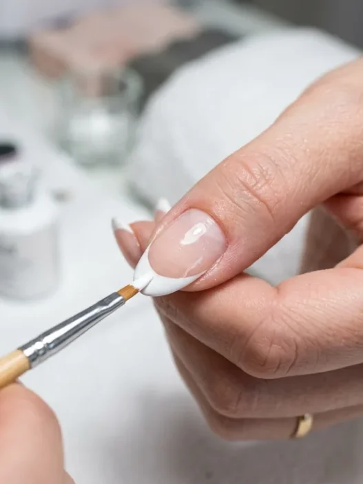 Close-up of precision brush applying white polish to create perfect French tip manicure