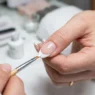 Close-up of precision brush applying white polish to create perfect French tip manicure