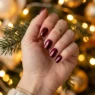 Close-up of burgundy chrome finished nails against warm golden fairy light bokeh background