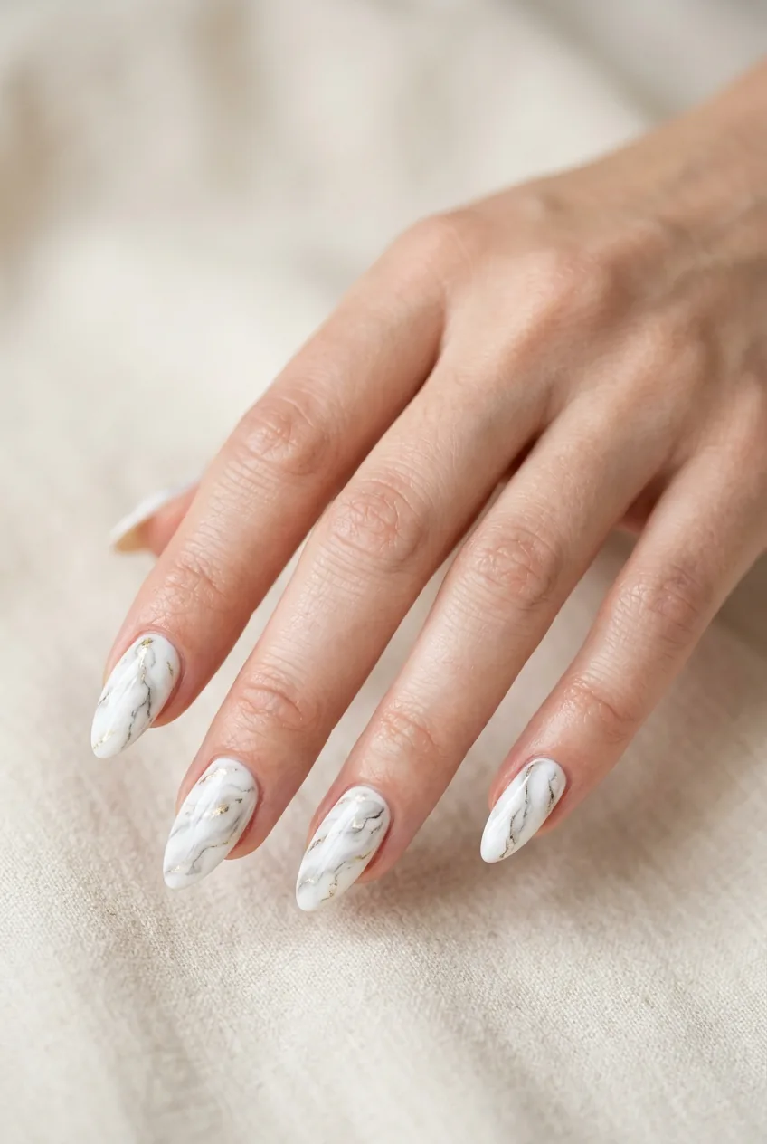 Woman's hand showing white marble effect almond nails with gray and gold veining patterns