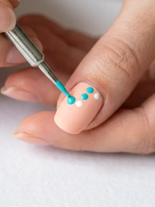 Metal dotting tool creating precise dot on pastel nail with existing pattern visible