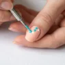 Metal dotting tool creating precise dot on pastel nail with existing pattern visible