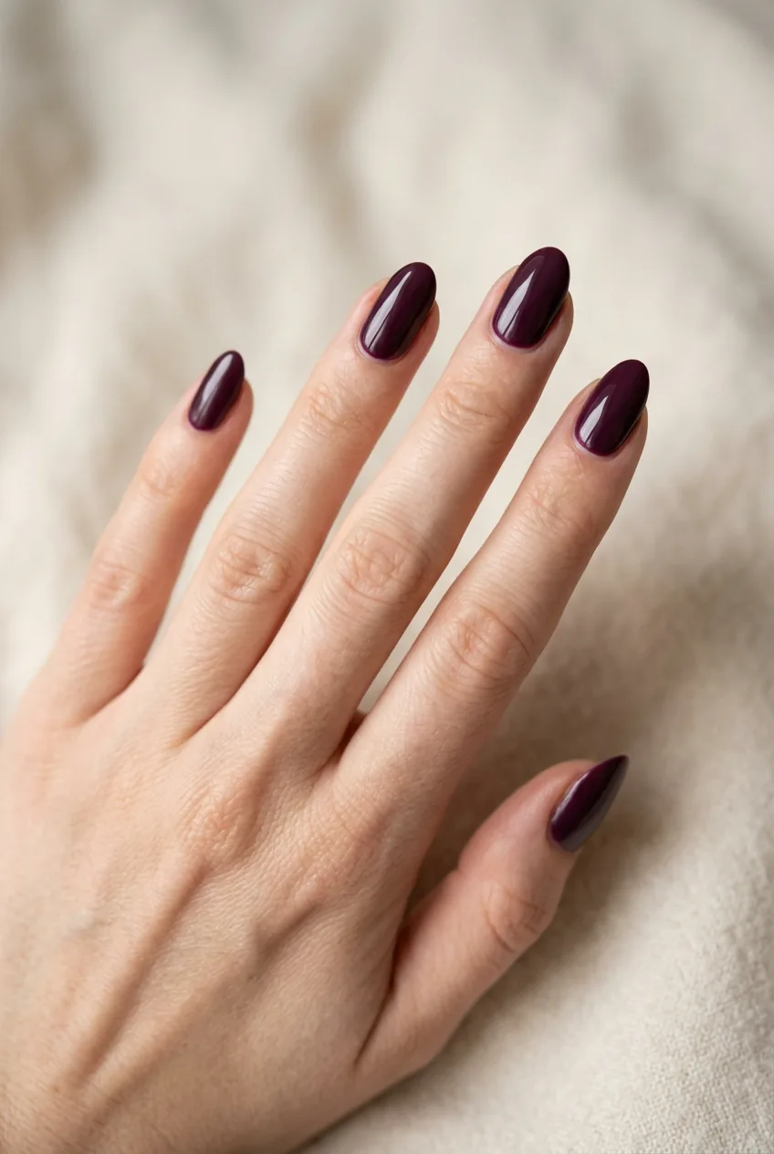 Woman's hand wearing moody plum statement manicure in deep burgundy-purple shade