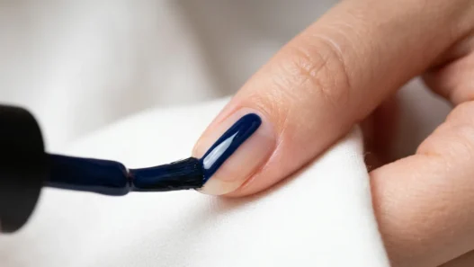 Polish brush applying glossy navy blue lacquer in single stroke down center of fingernail