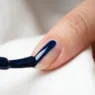 Polish brush applying glossy navy blue lacquer in single stroke down center of fingernail