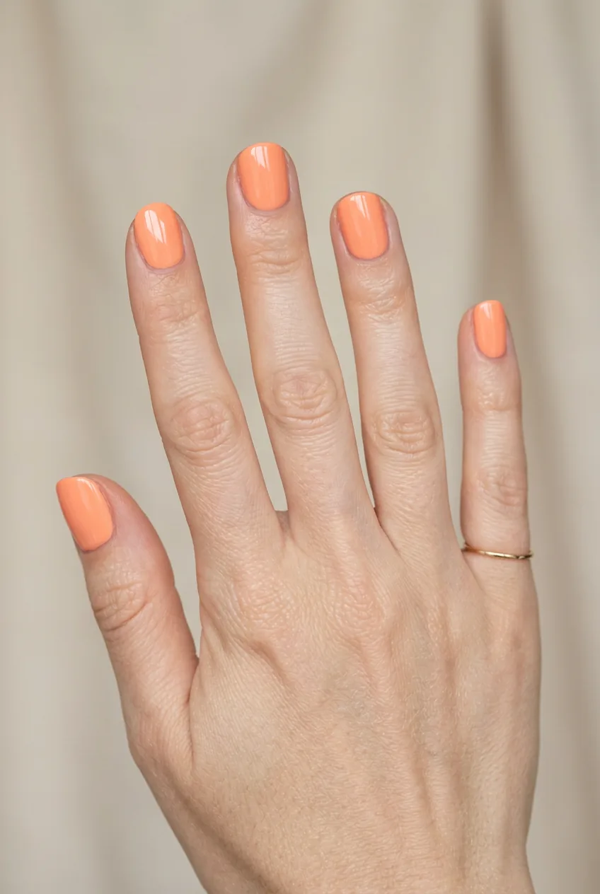 Woman's hand showing solid peachy orange summer manicure with glossy finish on short natural nails