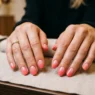 Woman's hands showing perfect pink to coral gradient nail art with glossy finish on salon table