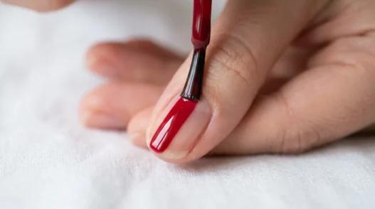 Macro close-up of nail polish brush applying glossy pink coat to center of nail with clean ribbon of color