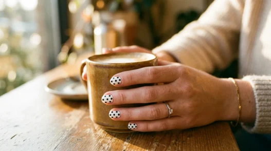 Woman's hand showing fresh black polka dots on white nail polish in natural golden hour lighting