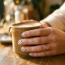 Woman's hand showing fresh black polka dots on white nail polish in natural golden hour lighting