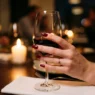 Manicured hand with classic red nails holding wine glass at candlelit dinner table
