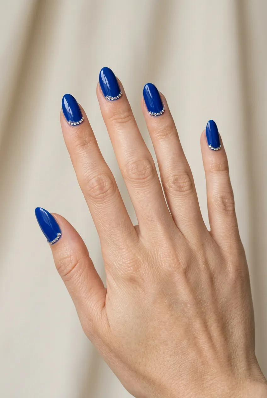 Woman's hand displaying royal blue nail polish with crystal rhinestones near cuticles