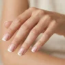 Woman's hand showing French manicure with white tips and nude pink base on short square nails