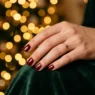 Manicured hands with winter nail polish against warm fairy lights creating golden bokeh background