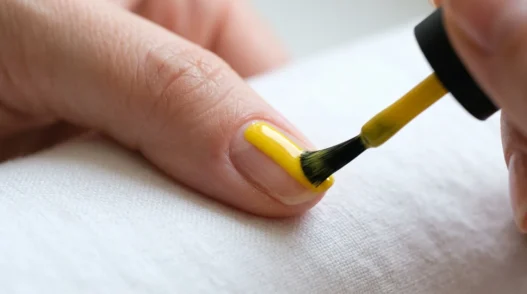 Polish brush applying glossy yellow nail polish in smooth center stroke on natural nail