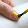 Polish brush applying glossy yellow nail polish in smooth center stroke on natural nail