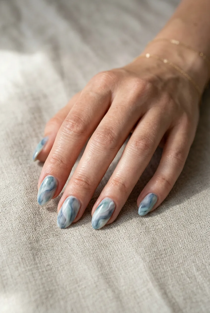 Woman's hand with nails featuring watercolor effect blending soft blues and grays in organic patterns