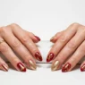 Woman's hands displaying completed Christmas nail art with red and gold festive design on salon table