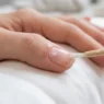 Close-up of clear base coat being brushed onto a freshly prepped nail resting on white silk in diffused daylight