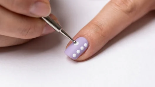 Metal dotting tool placing precise dot of polish on pastel nail with uniform dot pattern visible