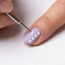 Metal dotting tool placing precise dot of polish on pastel nail with uniform dot pattern visible