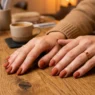 Woman's hands fanned elegantly on a salon table showing ten finished terracotta matte nails in warm amber lighting