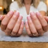 Woman's hands fanned elegantly on salon table showing ten completed french tip nails with glossy white tips