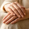 Woman's hands showing fresh natural manicure in soft nude polish against neutral background